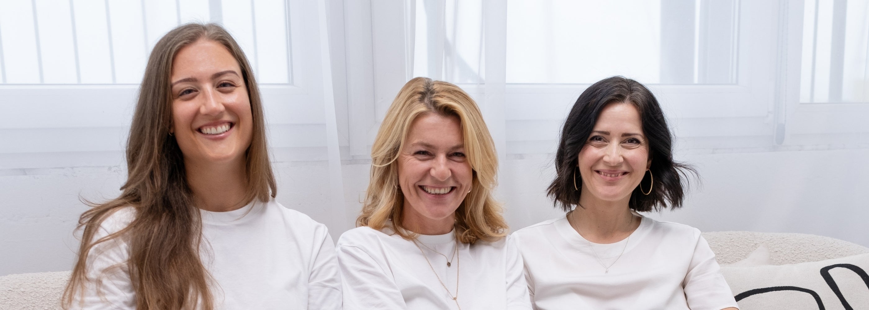 Drei Frauen, die Gründerinnen von FemBe, sitzen auf einer Couch in einem hellen Wohnzimmer Setting