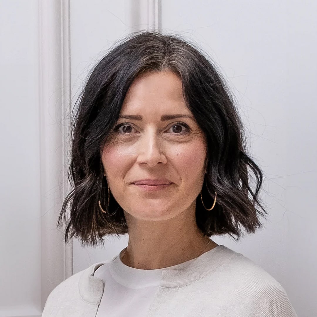 Eine dunkelhaarige Frau mit weißem T-Shirt im Portrait Modus, lächelt in die Kamera