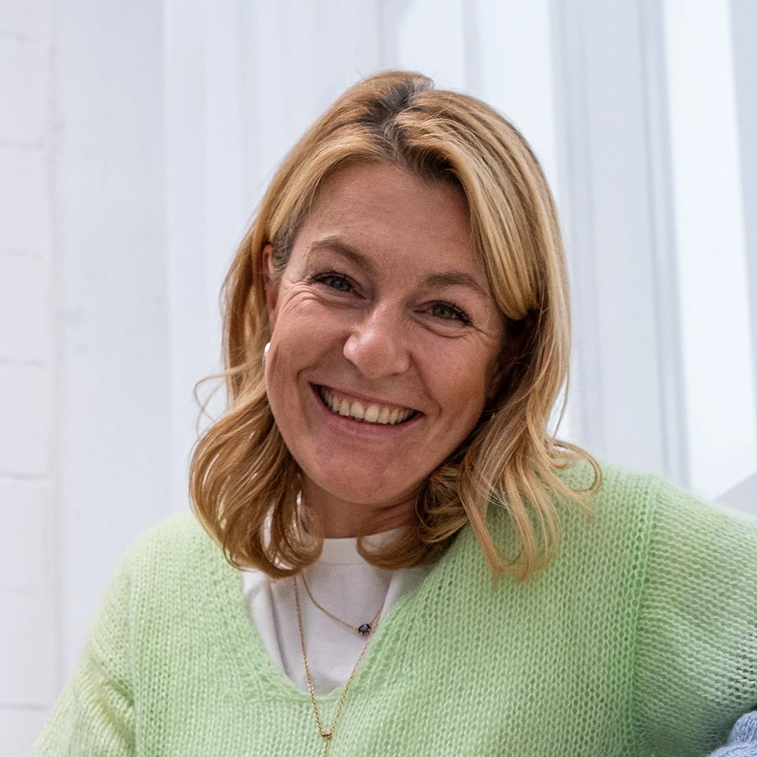 Eine blonde Frau mit weißem T-Shirt im Portrait Modus, lächelt in die Kamera